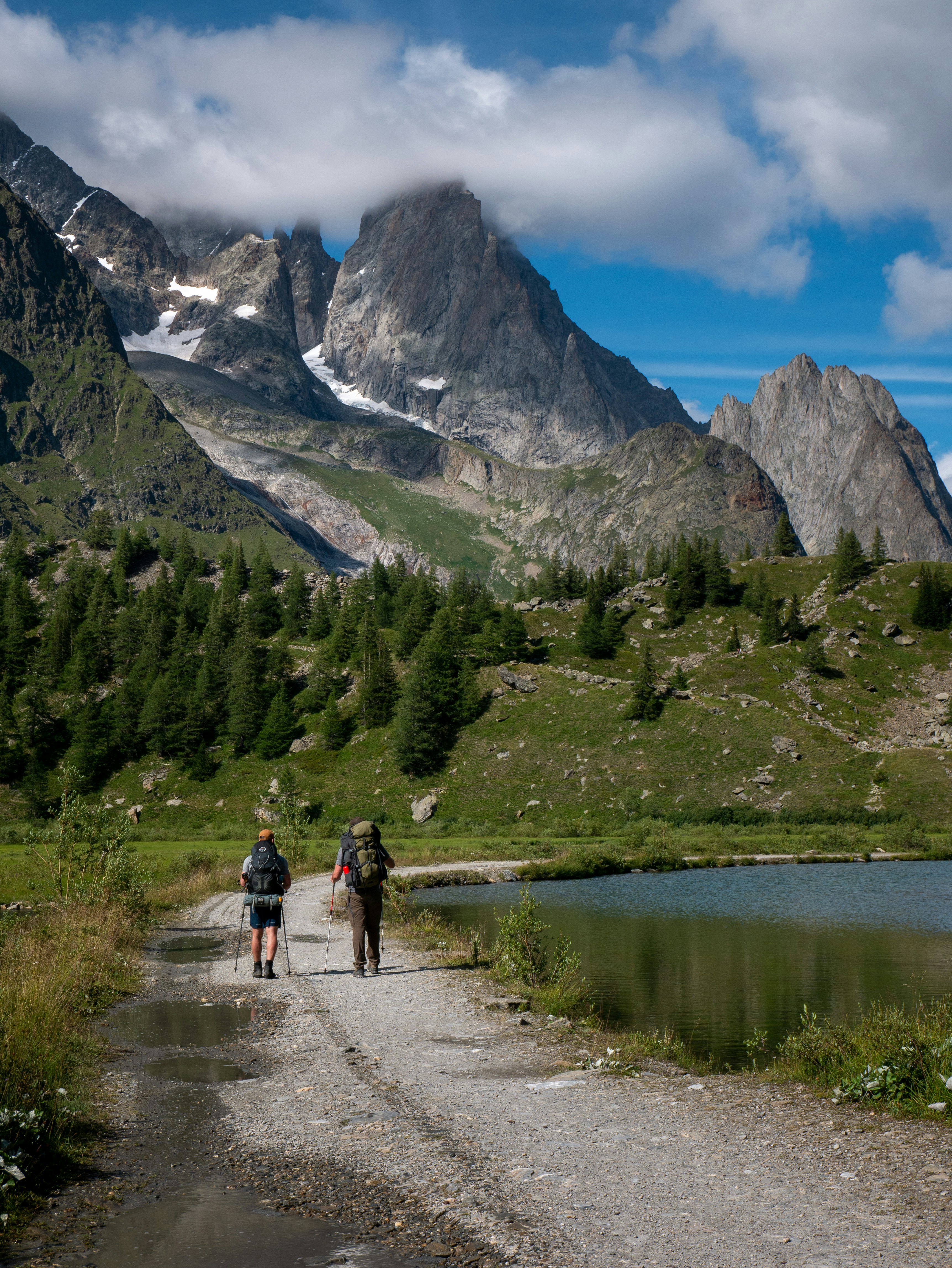 Hikers walking beside an alpine lake and meadow trail in the French Alps during summer